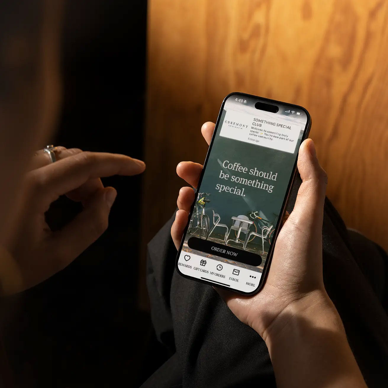 Person holding a smartphone with a coffee-themed app open, against a wooden wall.