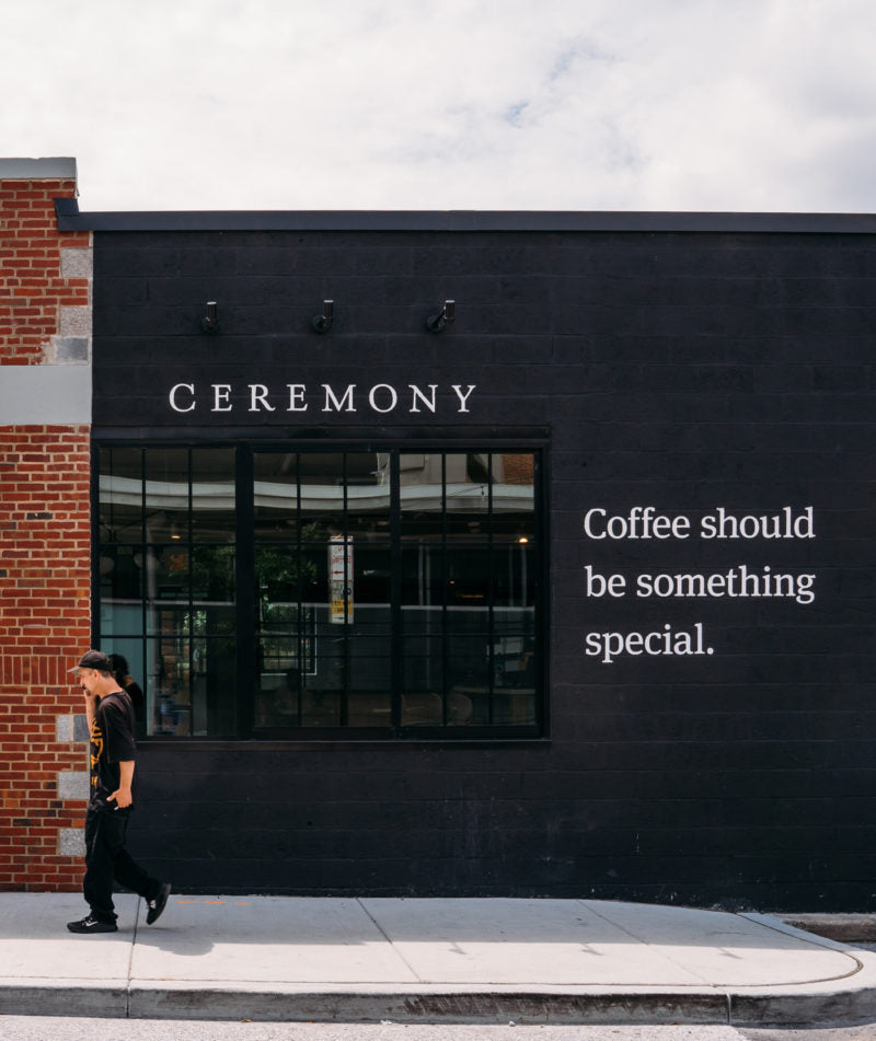 Customer walking outside Ceremony Cross Street location with the tag "Coffee should be something special" on the wall.